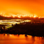 1507_JesseWinter_Wildfire_Story-3 Forest fires encroaching on a town, reflected in the water.