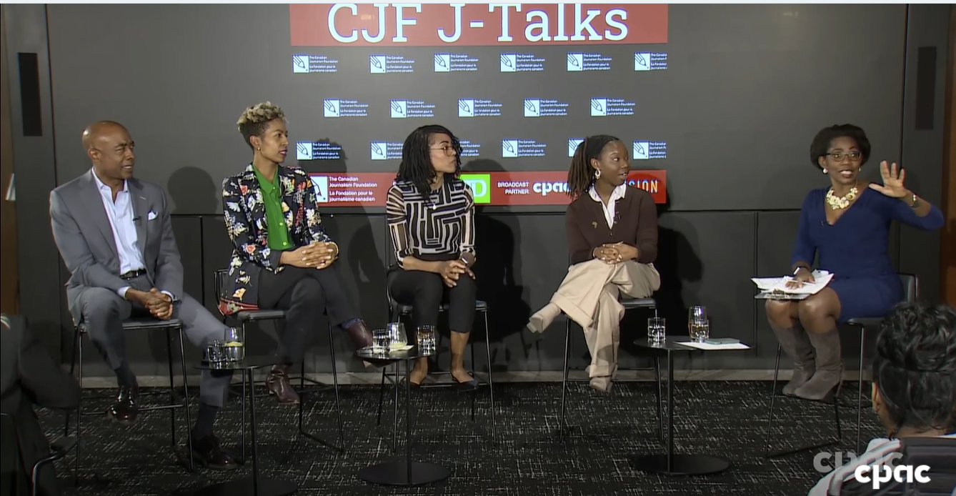 Left-to-right: Nathan Downer, Allya Davidson, Wendy-Ann Clarke, Dominique Gene and Andria Case sit at the front of a room. Andria Case is speaking and gesturing, while the other panelists look on.